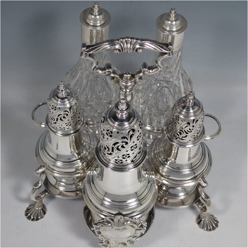 An Antique Georgian Sterling Silver and hand-cut crystal five-bottle Warwick style cruet set, having a stand with ring & scroll work holders, a cast loop handle with shell, a cast applied shell-style cartouche, and sitting on four cast shell feet. With two smaller baluster style pepper pots, a larger baluster sugar caster, and two hand-cut crystal oil & vinegar bottles with silver tops. Made by Samuel Woods of London in 1752-1754. The dimensions of this fine hand-made silver cruet set are width of stand 20 cms (8 inches), height of stand 23 cms (9 inches), and weight of silver approx. 1,500g (48 troy ounces). Please note that the silver tops on the crystal bottles are unmarked, and the stand is crested.