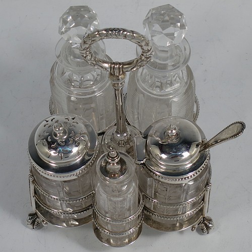 A very pretty Antique Victorian Sterling Silver table cruet set, consisting of two crystal bottles with original stoppers for oil and vinegar, a pepper shaker with crystal body and pierced silver lid, a salt/mustard pot with crystal body and silver hinged lid and condiment spoon, and a smaller bottle with silver serving spoon for a piquant sauce. All sitting in their original galleried frame with bead-edged borders, a cast laurel-leaf ring handle, and four cast claw and ball feet. Made by Martin Hall and Co., of Sheffield in 1868. The dimensions of this fine antique silver cruet set are height 15.5 cms (6 inches), and width 10 cms (4 inches).