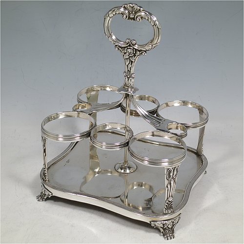 An Antique Georgian Sterling Silver large table cruet set, having a Regency style rectangular stand with an applied gadroon border, with ring handle and a frame for six hand-cut crystal cruet bottles with original stoppers and silver mounts, all sitting on a base with four cast lions paw feet. Made by William Bateman I of London in 1825. The dimensions of this fine antique silver cruet set are height 20 cms (8 inches), length 15 cms (6 inches), and width 13 cms (5 inches). Please note that the base has a wooden insert underneath.