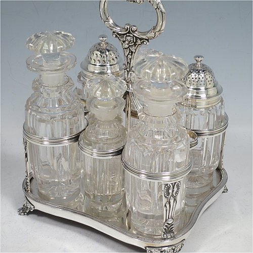 An Antique Georgian Sterling Silver large table cruet set, having a Regency style rectangular stand with an applied gadroon border, with ring handle and a frame for six hand-cut crystal cruet bottles with original stoppers and silver mounts, all sitting on a base with four cast lions paw feet. Made by William Bateman I of London in 1825. The dimensions of this fine antique silver cruet set are height 20 cms (8 inches), length 15 cms (6 inches), and width 13 cms (5 inches). Please note that the base has a wooden insert underneath.
