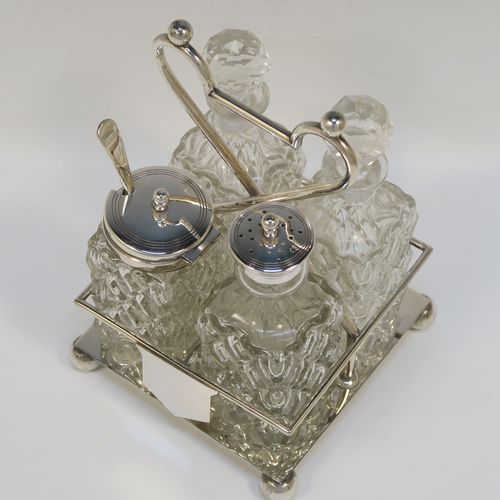 A handsome Antique Victorian Silver Plated and hand-cut crystal cruet set, having four crystal bottles with original stoppers and silver mounts, consisting of an oil and vinegar, a mustard pot spoon, and a pepper shaker, all sitting in a square galleried frame with a wire-work looped handle, and sitting on four cast ball feet. This original antique silver-plated cruet set was ca. 1870. The dimensions of this fine hand-made antique silver-plated cruet set are height of frame 19 cms (7.5 inches), and 11.5 cms (4.5 inches) square.