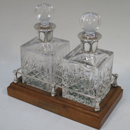 A very handsome pair of small Sterling Silver and hand-cut crystal decanters sitting in a galleried wood base, having square cross-section bodies with silver collars and original stoppers, all sitting in a silver galleried wooden base with green felt interiors. Made by Charles S. Green and Co. Ltd., of Birmingham in 1986. The dimensions of this fine pair of silver and crystal decanters (including base) are height 17 cms (6.75 inches), length 19 cms (7.5 inches), and width 10 cms (4 inches).