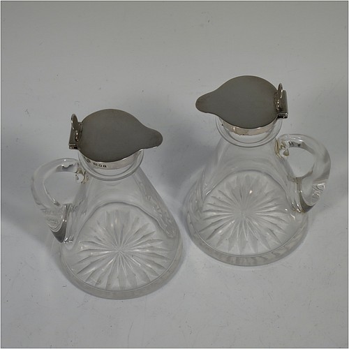 A Sterling Silver pair of whisky toddies or noggins, having round based hand-cut crystal bodies with tapering sides and loop handles, mounted with silver collars and hinged flat lids with thumb-pieces, all sitting on flat star-cut bases. Made by Goldsmiths and Silversmiths of London in 1932. The dimensions of this fine hand-made pair of silver and crystal noggins or toddies are height 11 cms (4.25 inches), and diameter at bases 6.5 cms (2.5 inches).   