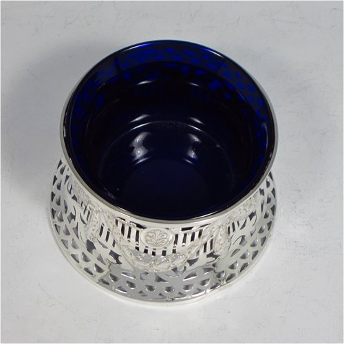 An Antique Edwardian Sterling silver miniature dish ring, having a hand-pierced and chased body with neoclassical style decoration, and a blue-glass liner. Made by Williams of Birmingham in 1910. The dimensions of this fine hand-made miniature silver dish ring are height 8 cms (2.3 inches), diameter at base 10 cms (4 inches), and it weighs approx. 85g (2.7 troy ounces).