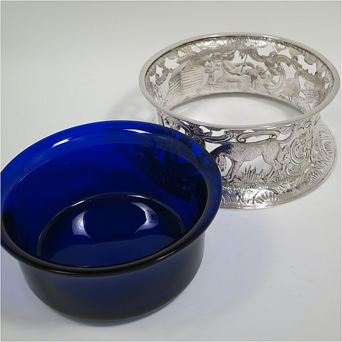 An Antique Victorian Sterling Silver large table dish ring in an Irish style, having a hand-pierced and chased body decorated with pastoral scenes, figures, animals, a vacant oval cartouche, and a blue-glass liner. Made by D. and J. Welby of London in 1894. The dimensions of this fine hand-made antique silver dish ring are height 7.5 cms (3 inches), diameter at base 19 cms (7.5 inches), and it weighs approx. 351g (11.3 troy ounces).