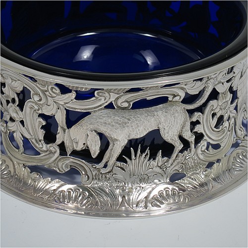 An Antique Victorian Sterling Silver large table dish ring in an Irish style, having a hand-pierced and chased body decorated with pastoral scenes, figures, animals, a vacant oval cartouche, and a blue-glass liner. Made by D. and J. Welby of London in 1894. The dimensions of this fine hand-made antique silver dish ring are height 7.5 cms (3 inches), diameter at base 19 cms (7.5 inches), and it weighs approx. 351g (11.3 troy ounces).