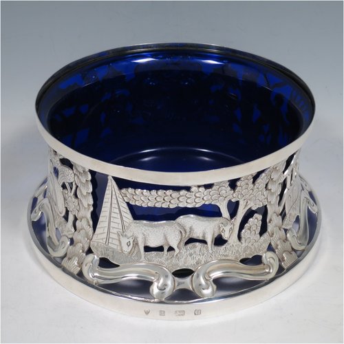 An Antique Edwardian Sterling Silver large table dish ring in an Irish style, having a hand-pierced and chased body decorated with pastoral scenes, figures, and animals, and a blue-glass liner. Made by Israel Sigmund Greenberg of Birmingham in 1904. The dimensions of this fine hand-made antique silver dish ring are height 10 cms (4 inches), diameter at base 20 cms (8 inches), and it weighs approx. 387g (12.5 troy ounces).    