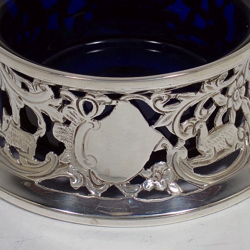 A handsome Antique Victorian Sterling silver miniature dish ring, in an Irish style, having a hand-pierced and chased body with with pastoral scenes, figures, animals, a vacant oval cartouche, and a blue-glass liner. Made by John and Frank Pairpoint of London in 1901. The dimensions of this fine hand-made antique miniature silver dish ring are height 5 cms (2 inches), diameter at base 11 cms (4.3 inches), and it weighs approx. 108g (3.5 troy ounces).