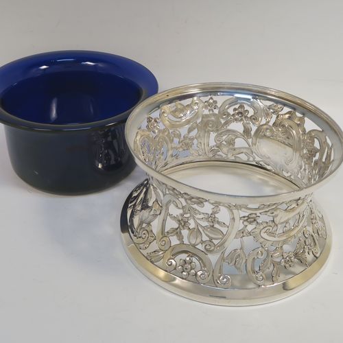 A very beautiful Irish Antique Sterling Silver large table dish ring, having a hand-pierced and chased body decorated with scrolls, flowers, and animals, a single vacant cartouche, and a blue-glass liner. This elegant silver potato or dish ring was made by West and Son of Dublin in 1917. The dimensions of this fine hand-made antique silver dish ring are height 10 cms (4 inches), diameter at base 18.5 cms (7.25 inches), and it weighs approx. 326g (10.5 troy ounces).