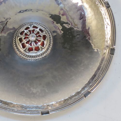 A very beautiful Sterling Silver Arts and Crafts table dish, having a round hand-hammered body, with an applied reed cog border, a central Tudor Rose style boss with an applied rope-twist border and dark red enamel underneath showing through the piercing, and all sitting on a collet foot. Made by Omar Ramsden of London in 1923. The dimensions of this fine hand-made Arts and Crafts silver dish are diameter 11 cms (4.3 inches), and it weighs approx. 93g (3 troy ounces).