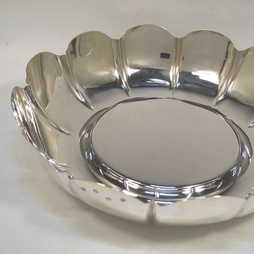 A very large, heavy, and handsome Sterling Silver strawberry dish, having a plain round body, with a raised flat ground, melon fluted sides with hand-chased lobed edges. This elegant silver dish was made by the Royal Irish Silver Co., of London in 1973. The dimensions of this fine hand-made table dish are diameter 33 cms (13 inches), height 8.5 cms (3.3 inches), and it weighs approx. 1,302g (42 troy ounces).