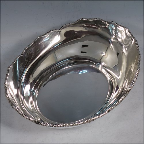 An Antique Edwardian Sterling Silver bread roll table dish, having an oval plain body with an applied wavey-edged rope-twist or gadroon border, and sitting on a flat base. Made by William Hutton & Sons of Sheffield in 1908. The dimensions of this fine hand-made antique silver bread dish are length 20 cms (8 inches), width 15 cms (6 inches), height 7 cms (2.75 inches), and it weighs approx. 285g (9.2 troy ounces).