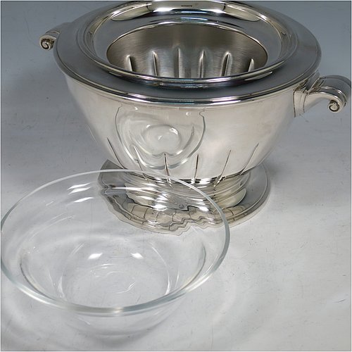 A Sterling Silver Caviar serving dish in an Art Deco style, having a round body with hand-chased straight half-fluting, with two cast scroll side-handles, a removable glass bowl that sits on a rim below which crushed ice can be added, and sitting on a matching pedestal foot. Made by Aspreys & Garrards of London in 2000. The dimensions of this fine hand-made silver caviar serving dish are 17 cms (6..75 inches) diameter, height 11.5 cms (4.5 inches), and it weighs approx. 840g (27 troy ounces).
