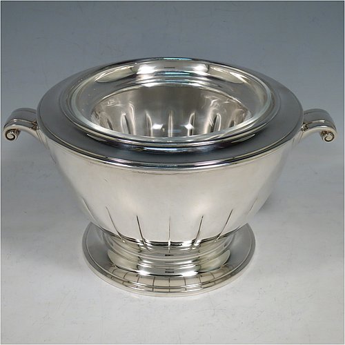 A Sterling Silver Caviar serving dish in an Art Deco style, having a round body with hand-chased straight half-fluting, with two cast scroll side-handles, a removable glass bowl that sits on a rim below which crushed ice can be added, and sitting on a matching pedestal foot. Made by Aspreys & Garrards of London in 2000. The dimensions of this fine hand-made silver caviar serving dish are 17 cms (6..75 inches) diameter, height 11.5 cms (4.5 inches), and it weighs approx. 840g (27 troy ounces).