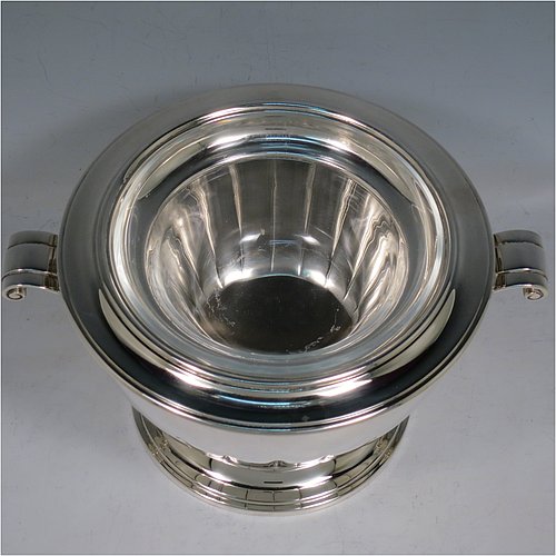 A Sterling Silver Caviar serving dish in an Art Deco style, having a round body with hand-chased straight half-fluting, with two cast scroll side-handles, a removable glass bowl that sits on a rim below which crushed ice can be added, and sitting on a matching pedestal foot. Made by Aspreys & Garrards of London in 2000. The dimensions of this fine hand-made silver caviar serving dish are 17 cms (6..75 inches) diameter, height 11.5 cms (4.5 inches), and it weighs approx. 840g (27 troy ounces).