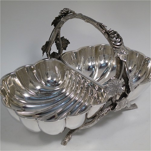 An Antique Victorian Silver Plated very unusual double shell bread roll or biscuit dish, having two connected side dishes with hand-chased shell style decoration, with a central cast vine-leaf and tendril handle, and sitting on four cast branch-like feet. Made by Mappin and Webb in their Princes Plate in ca. 1880. The dimensions of this fine hand-made antique silver-plated biscuit or bread roll dish are length 30 cms (11.75 inches), width 20 cms (8 inches), and height 17 cms (6.75 inches).