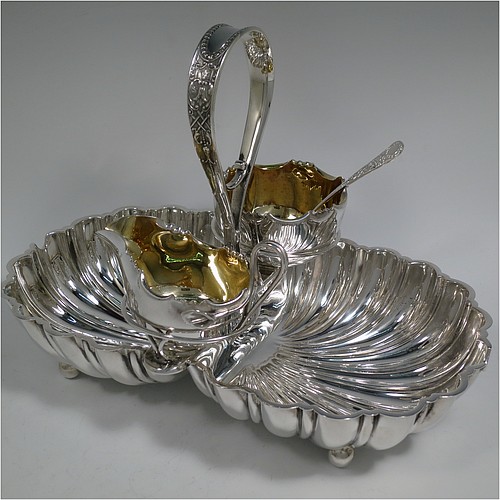An Antique Victorian Silver-Plated strawberry dish, having two melon-fluted fixed shell dishes, a removable sugar bowl and cream jug both with gold-gilt interiors, an original sugar sifting ladle, and all sitting in a frame with loop handle and four ball feet. Made by James Dixon and Sons of Sheffield in ca. 1880. The dimensions of this fine hand-made antique silver-plated double strawberry dish are length 32 cms (12.5 inches), width 20 cms (8 inches), and height 22 cms (8.75 inches).