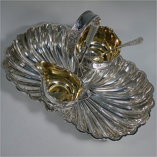 An Antique Victorian Silver-Plated strawberry dish, having two melon-fluted fixed shell dishes, a removable sugar bowl and cream jug both with gold-gilt interiors, an original sugar sifting ladle, and all sitting in a frame with loop handle and four ball feet. Made by James Dixon and Sons of Sheffield in ca. 1880. The dimensions of this fine hand-made antique silver-plated double strawberry dish are length 32 cms (12.5 inches), width 20 cms (8 inches), and height 22 cms (8.75 inches).