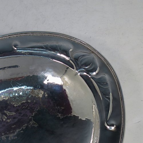 A Sterling Silver Arts and Crafts style dish, having an oval body with hand-hammered decoration, an applied rope-twist border, with hand-chased floral and scroll work at either ends, and all sitting on a collet foot. Made by Henry Charles Hall (from the Swansea School of Crafts) of Sheffield in 1932. The dimensions of this fine hand-made silver table dish are length 31 cms (12.25 inches), width 21 cms (8.25 inches), height 4 cms (1.5 inches), and it weighs approx. 464g (15 troy ounces).