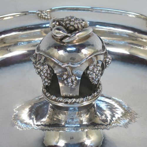 A very elegant and unusual Sterling Silver Arts and Crafts style large table fruit dish, having a round hand-hammered body, a central handle with cast grape and fruit decoration, and an applied grape border. Made by A. E. Jones of Birmingham in 1936. The dimensions of this fine hand-made silver fruit dish are diameter 31 cms (12.25 inches), height 10 cms (4 inches), and it weighs approx. 1,080g (34.8 troy ounces).