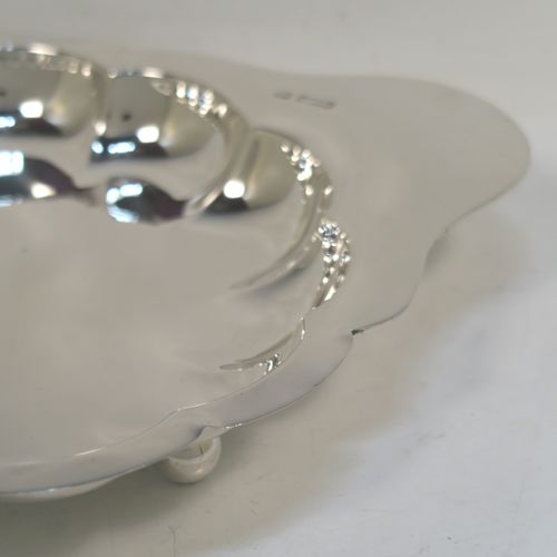 An elegant Antique Edwardian Sterling Silver strawberry dish, having a plain round body with a hand-chased lobed border, a plain side handle, and all sitting on three ball feet. This handsome antique silver strawberry dish was made by the Atkins Brothers of Sheffield in 1905. The dimensions of this fine hand-made antique silver dish are length 25 cms (9.75 inches), diameter of main body 20 cms (8 inches), and it weighs approx. 293g (9 troy ounces).