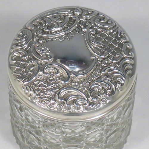 An Antique Victorian Sterling Silver and cut-crystal dressing table jar / box, having a round hand-cut crystal body in the Hobnail pattern, a hand-chased pull-off lid with floral decoration, and sitting on a flat star-cut base. Made by Adie & Lovekin Ltd., of Birmingham in 1901. The dimensions of this fine hand-made antique silver and crystal dressing table box / jar are height 8 cms (3 inches), and diameter 7 cms (2.75 inches).   