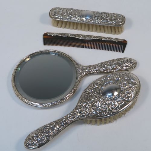 A very pretty Sterling Silver four-piece dressing table, consisting of a hand-mirror with a bevelled mirror, a hair brush, a clothes brush, and a hand comb, all hand-chased with floral and scroll decoration, with nylon bristles, and in their original cream satin-lined and blue presentation box. This beautiful silver dressing table set was made in Birmingham in 2002. The dimensions of this fine hand-made sterling silver dressing table service are length of hand mirror 24 cms (9.5 inches), length of hair brush 23 cms (9 inches), and length of clothes brush 15 cms (6 inches).
