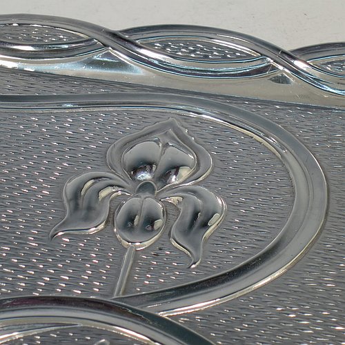 An Antique Edwardian Sterling Silver Arts and Crafts style dressing table pin tray, having a a shaped rectangular body with hand-chased scroll-work and lillies in a Rennie Mackintosh style, with a central vacant cartouche, and all sitting on a flat base. Made by A & J Zimmerman of Birmingham in 1902. The dimensions of this fine hand-made antique silver pin tray are length 33 cms (13 inches), width 22 cms (8.75 inches), and it weighs approx. 403g (13 troy ounces).    