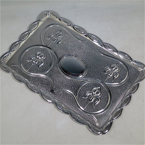 An Antique Edwardian Sterling Silver Arts and Crafts style dressing table pin tray, having a a shaped rectangular body with hand-chased scroll-work and lillies in a Rennie Mackintosh style, with a central vacant cartouche, and all sitting on a flat base. Made by A & J Zimmerman of Birmingham in 1902. The dimensions of this fine hand-made antique silver pin tray are length 33 cms (13 inches), width 22 cms (8.75 inches), and it weighs approx. 403g (13 troy ounces).    