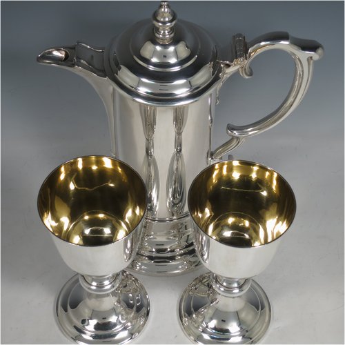 An Antique Victorian Sterling Silver communion service composed of a flagon and two goblets. The flagon in an early 17th century style having a straight-sided body, a scroll handle, a hinged & domed lid with urn-shaped finial, a matching scrolled spout and sitting on a collet foot. Together with a pair of plain round baluster goblets with gold-gilt interiors. All made by Robert Garrard of London in 1862/63. The dimensions of this fine hand-made communion set are height of flagon 29 cms (11.5 inches), length across handle & spout 23 cms (9 inches), height of goblets 18 cms (7 inches), and with a total weight of approx. 1,643g (53 troy ounces).