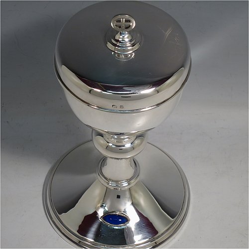 A Sterling Silver Ciborium, having a plain round body, sitting on a matching pedestal foot with an applied oval dark blue cabochon stone, with reeded borders, and a lift-off lid with cruciform finial. Made by Frederick Osborne & Co., of Birmingham in 1930. The dimensions of this fine hand-made silver ciborium are height 20 cms (8 inches), diameter of cup 9.5 cms (3.75 inches), and it weighs a total of approx. 385g (12.5 troy ounces).