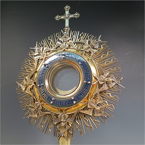 An Antique Victorian Sterling Silver and gold-gilt Monstrance, having a cruciform finial over a central Lunar receptacle in an elaborate sun-ray frame with eight applied winged angels, all mounted on a pedestal foot with hand-chased vine-leaf central knop over a hexafoil base. All decorated with 39 old cut foil-backed diamonds (one missing), 15 pearls of good lustre and uneven shape, a blue-enamelled Lunar surround engraved with the Latin Sanctus repeated, and 27 set turquoise stones. Made by John Harman & Co., of Birmingham in 1899. The dimensions of this fine hand-made antique silver and gold-gilt Monstrance are height 68 cms (26.75 inches), width 29 cms (11.5 inches), depth 25.5 cms (10 inches), and it weighs approx. 2,800g (90 troy ounces). Please note that the overall total estimated diamond weight is 5.5 carats).