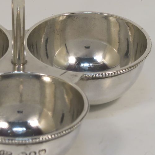 An elegant Antique Victorian Sterling Silver egg cruet or holder set, having three attached plain round bodied egg cups with applied bead-edged borders, and a ring handle above. This handsome antique egg holder was made by Heath and Middleton of London in 1889. The dimensions of this fine hand-made silver egg holder are height 10 cms (4 inches), width 10 cms (4 inches), and it weighs approx. 82g (2.6 troy ounces).