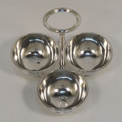 An elegant Antique Victorian Sterling Silver egg cruet or holder set, having three attached plain round bodied egg cups with applied bead-edged borders, and a ring handle above. This handsome antique egg holder was made by Heath and Middleton of London in 1889. The dimensions of this fine hand-made silver egg holder are height 10 cms (4 inches), width 10 cms (4 inches), and it weighs approx. 82g (2.6 troy ounces).
