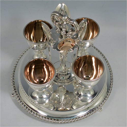 A very pretty Antique Victorian Sterling Silver egg cruet set, having a round body with applied gadroon borders, four plain round egg cups sitting on pedestal feet, and a cast loop handle attached to a round base sitting on four flange feet. Made by Andrew Crespel and Thomas Parker of London in 1867. The matching spoons are made by Jackson & Fullerton of London in 1906. The spoon and egg cup bowl interiors are all gold-gilt. The dimensions of this fine hand-made antique silver egg cruet set are height 18 cms (7 inches), diameter of base 17 cms (6.75 inches), and the total weight is approx. 856g (27.6 troy ounces). Please note that all items in this set are crested.