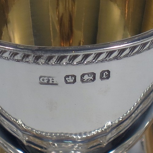 An Antique Victorian Sterling Silver egg cruet set, having four plain round egg cups with gold-gild interiors sitting on pedestal feet, four egg spoons with gold-gilt bowls, and a plain cast loop handle attached to a round base with an applied shaped gadroon border, and sitting on four cast scroll feet. Made by George Hancock of Sheffield in 1897 (the spoons by James Dixon and Sons of Sheffield in 1917). The dimensions of this fine hand-made antique silver egg cruet set are height 20 cms (8 inches), diameter of base is 15 cms (6 inches), and the total weight is approx. 688g (22 troy ounces).