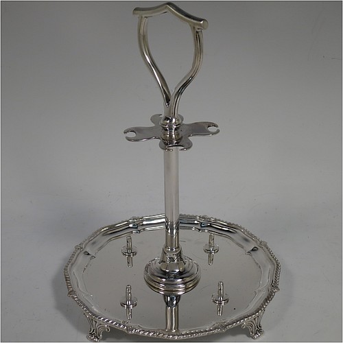 An Antique Victorian Sterling Silver egg cruet set, having four plain round egg cups with gold-gild interiors sitting on pedestal feet, four egg spoons with gold-gilt bowls, and a plain cast loop handle attached to a round base with an applied shaped gadroon border, and sitting on four cast scroll feet. Made by George Hancock of Sheffield in 1897 (the spoons by James Dixon and Sons of Sheffield in 1917). The dimensions of this fine hand-made antique silver egg cruet set are height 20 cms (8 inches), diameter of base is 15 cms (6 inches), and the total weight is approx. 688g (22 troy ounces).