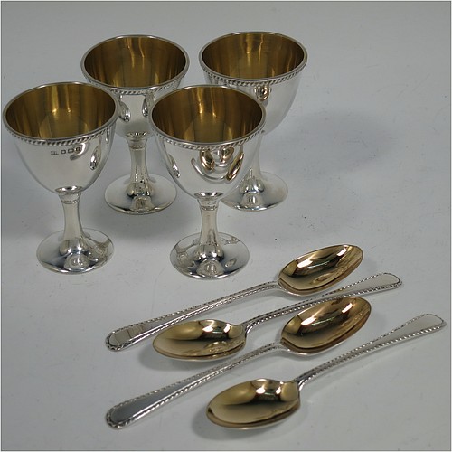 An Antique Victorian Sterling Silver egg cruet set, having four plain round egg cups with gold-gild interiors sitting on pedestal feet, four egg spoons with gold-gilt bowls, and a plain cast loop handle attached to a round base with an applied shaped gadroon border, and sitting on four cast scroll feet. Made by George Hancock of Sheffield in 1897 (the spoons by James Dixon and Sons of Sheffield in 1917). The dimensions of this fine hand-made antique silver egg cruet set are height 20 cms (8 inches), diameter of base is 15 cms (6 inches), and the total weight is approx. 688g (22 troy ounces).