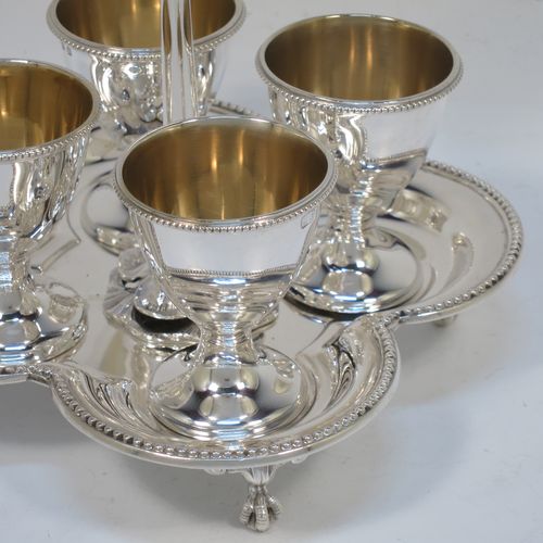 A very pretty Antique Victorian Sterling Silver egg cruet set, having four plain round egg cups with bead borders and gold-gild interiors sitting on pedestal feet, together with a cast laurel leaf loop handle attached to a lobed base with an applied bead-edged border, and all sitting on four cast claw and ball feet. Made by Elkington and Co., of Birmingham in 1866. The dimensions of this fine hand-made antique silver egg cruet set are height 18 cms (7 inches), width of base is 16.5 cms (6.5 inches), and the total weight is approx. 500g (16 troy ounces).