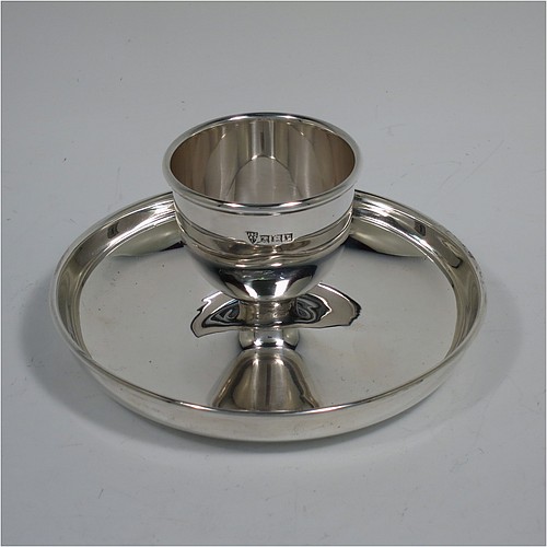 A Sterling Silver egg cup, having a plain round body with tapering sides, with an attached plain round plate with curved border, and sitting on a flat base. Made J. B. Chatterly of Birmingham in 1964. The dimensions of this fine hand-made silver egg cup are height 5 cms (2 inches), diameter 10 cms (4 inches), and it weighs approx. 87g (2.8 troy ounces).   