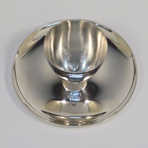 A Sterling Silver egg cup and plate, having a plain round body with tapering sides, with an attached plain round plate with curved border, and sitting on a flat base. This elegant silver egg cup was made by James Dixon Sons of Sheffield in 1943. The dimensions of this fine hand-made silver egg cup are height 4 cms (1.5 inches), diameter 9.5 cms (3.75 inches), and it weighs approx. 77g (2.5 troy ounces).