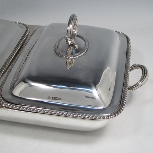 Sterling silver pair of entree dishes with covers and handles, sitting in an original plain rectangular hot-water warming frame, with applied gadroon borders and hand-pierced liners, having cast side-handles, and all sitting on four cushion feet. Made by D. & J. Wellby of London in 1916. The dimensions of this fine hand-made silver entree dish set are length 36 cms (14 inches), width 20 cms (8 inches), height including cover handles 12 cms (4.75 inches), and it weighs a total of approx. 1,965g (63 troy ounces).
