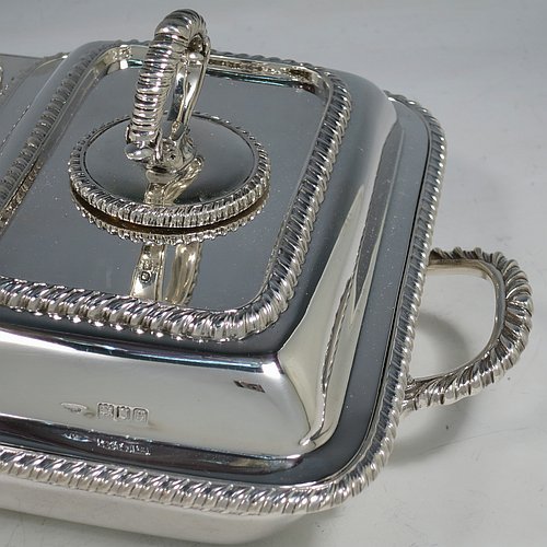 An Antique Edwardian Sterling Silver pair of entree dishes with covers on a silver-plated warming stand for hot water, having rectangular bodies with applied gadroon borders, and with removable bayonet-fit handles. All in original condition and made by Goldsmiths & Silversmiths of London in 1902. The dimensions of this fine pair of hand-made antique silver entree dishes on a silver plated warming stand are length (inc. handles) 34 cms (13.5 inches), width 20 cms (8 inches), height 12 cms (5 inches), and the entree dishes weigh approx. 1,721g (55.5 troy ounces).