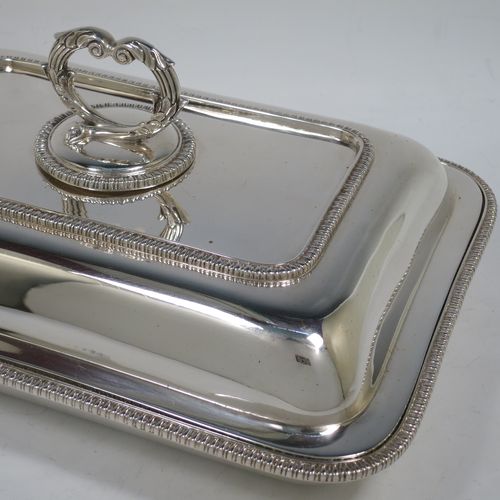 A handsome Antique Sterling Silver entree dish with cover, having a rectangular body with rounded corners and applied straight gadroon borders, a cast bayonet-fit removable asparagus style loop handle, and sitting on a flat base. Made by Carrington and Co., of London in 1912. The dimensions of this fine hand-made antique silver entree dish and cover are length 28 cms (11 inches), height including handle 11 cms (4.5 inches), width 20 cms (8 inches), and with a total weight of approx. 1,540g (49.7 troy ounces).