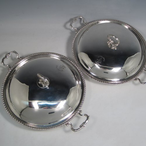 Antique Georgian sterling silver pair of entree or hash dishes with covers, having round bodies with applied gadroon borders and cast scroll side-handles, with plain domed lift-off covers having cast asparagus handles, an all sitting on flat bases. Made by Charles Wright of London in 1771. The dimensions of this pair of fine hand-made antique silver entree dishes and covers are diameter 24 cms (9.5 inches), height including cover handle 10 cms (4 inches), and they weigh a total of approx. 1,738g (56 troy ounces). Please note that both the bases and covers are crested.