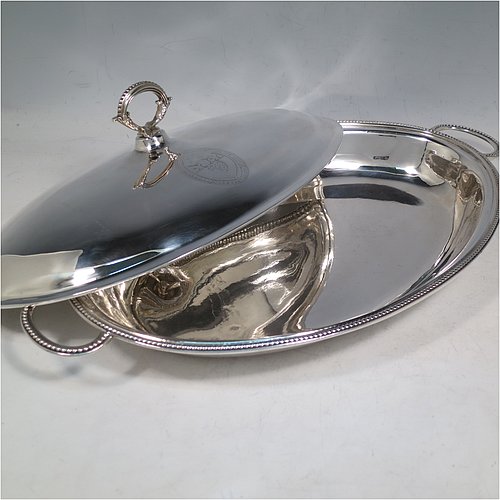An Antique Georgian Sterling Silver pair of entree or hash dishes with covers, having oval bodies with applied bead-edged borders and cast loop side-handles, with plain domed lift-off covers having removable cast bead handles, and all sitting on flat bases. Made by Henry Green of London in 1790. The dimensions of this pair of fine hand-made antique silver entree dishes and covers are length 38 cms (15 inches), width 21.5 cms (8.5 inches), height including cover handle 11 cms (4.3 inches), and they weigh a total of approx. 2,077g (67 troy ounces). Please note that both the bases and covers are crested.
