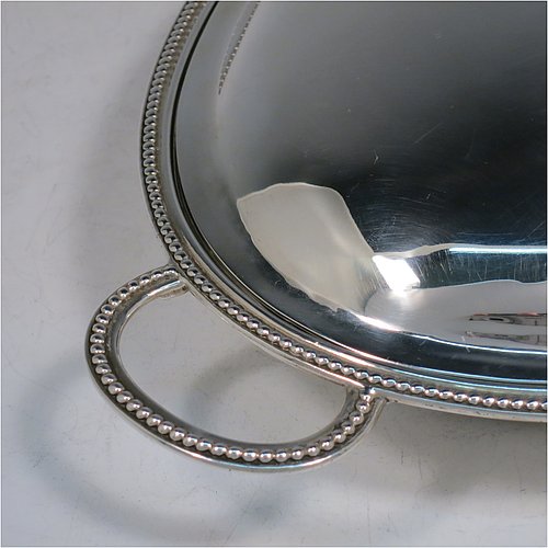 An Antique Georgian Sterling Silver pair of entree or hash dishes with covers, having oval bodies with applied bead-edged borders and cast loop side-handles, with plain domed lift-off covers having removable cast bead handles, and all sitting on flat bases. Made by Henry Green of London in 1790. The dimensions of this pair of fine hand-made antique silver entree dishes and covers are length 38 cms (15 inches), width 21.5 cms (8.5 inches), height including cover handle 11 cms (4.3 inches), and they weigh a total of approx. 2,077g (67 troy ounces). Please note that both the bases and covers are crested.