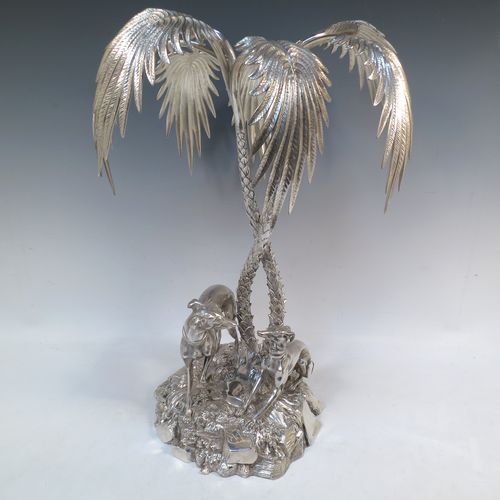 A very handsome Antique Victorian silver-plated table palm tree center-piece, having two palm trees inter-twined with a total of seven fronds, standing underneath which are two cast models of playful greyhounds or lurchers, and all sitting on a round naturalistic cast rock base. Made by Elkington and Co. with a date letter mark for 1852. The dimensions of this fine hand-made silver-plated table centerpiece display are height 41 cms (16 inches), spread across fronds 31 cms (12.25 inches), and diameter at base 20 cms (8 inches).

  