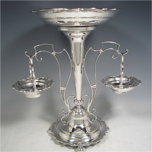 A Sterling Silver table Epergne centrepiece, having a removable central bowl, with two removable dishes on side arms, with applied scroll borders, an Art Nouveau style frame, and sitting on a spreading round base with four cushion feet. Made by the Deakin Brothers of Sheffield in 1924. The dimensions of this fine hand-made silver Epergne table centrepiece are height 32.5 cms (12.75 inches), width across arms 32 cms (12.5 inches), and it weighs a total of approx. 1,166g (37.6 troy ounces)   