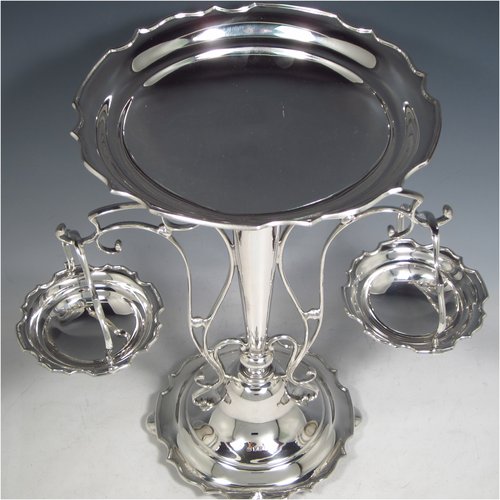 A Sterling Silver table Epergne centrepiece, having a removable central bowl, with two removable dishes on side arms, with applied scroll borders, an Art Nouveau style frame, and sitting on a spreading round base with four cushion feet. Made by the Deakin Brothers of Sheffield in 1924. The dimensions of this fine hand-made silver Epergne table centrepiece are height 32.5 cms (12.75 inches), width across arms 32 cms (12.5 inches), and it weighs a total of approx. 1,166g (37.6 troy ounces)   